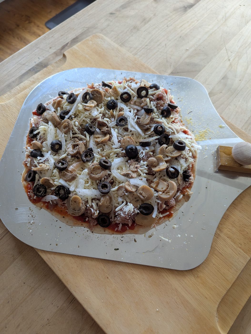 Uncooked Hup's-style pizza with sausage, mushrooms, onions, olives, and cheese on a peel