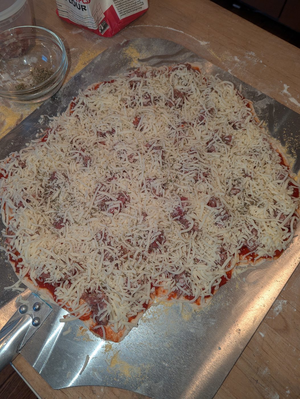 Pizza generously covered with shredded mozzarella, sausage visible underneath